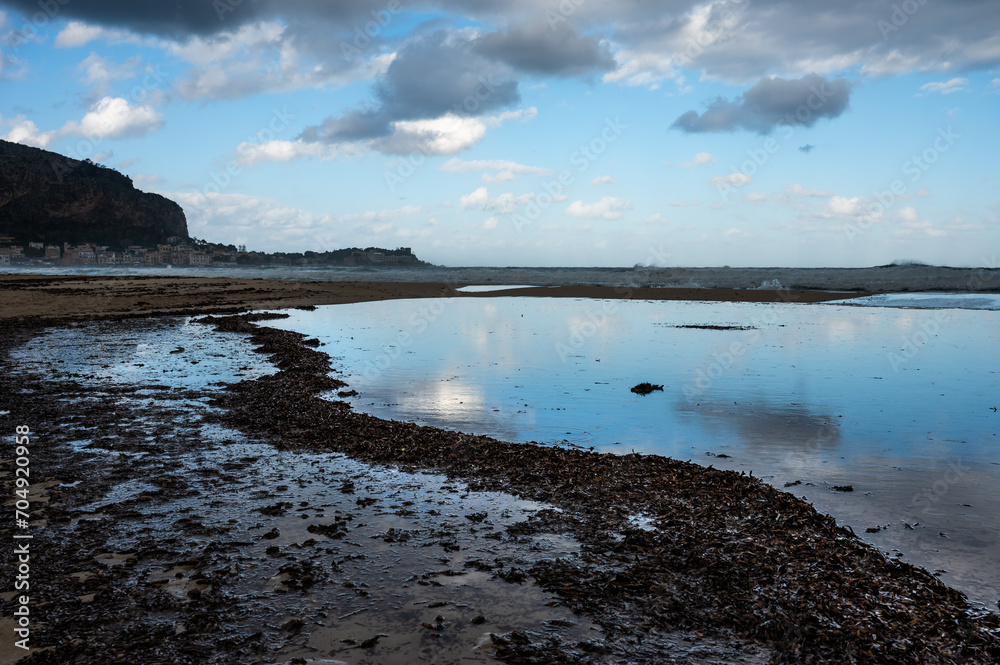 Dark rainy clouds reflecting in the water ponds at the beach of Mondello, -Italy