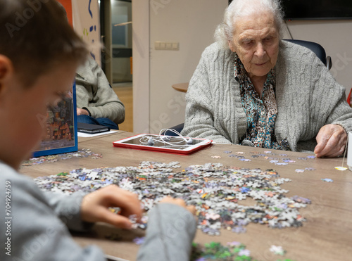 Great-grandmother playing with her great-grandson to do a puzzle photo