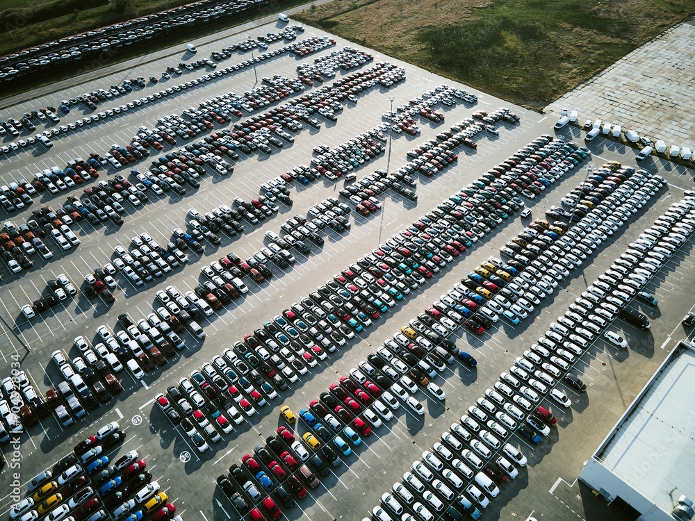 Obraz premium Aerial view of a massive parking lot at a car manufacturing facility with newly produced vehicles parked in rows.