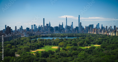 Aerial Helicopter Footage Over Central Park with Nature  Trees  People Having Picnic and Resting on a Field Around Manhattan Skyscrapers Cityscape. Beautiful Sunny Day. Slow Motion Footage