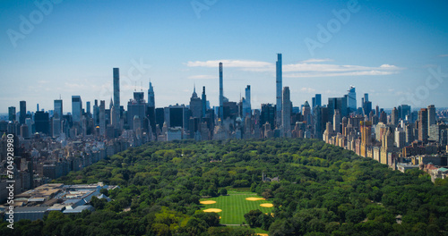 New York City Aerial Landscape Over Central Park with Midtown Manhattan Skyscrapers. Cinematic Drone View of Urban Skyline with Slightly Cloudy Blue Sky