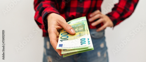 One hundred euro bills in hand of female person wearing red casual shirt. Giving money.