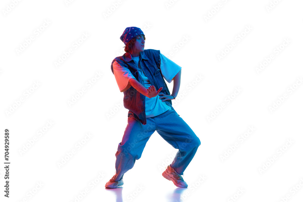 Dynamic image of young girl in casual sportive cloths dancing hip hop isolated over white background in neon light. Concept of contemporary dance, street style, youth, hobby, action, lifestyle