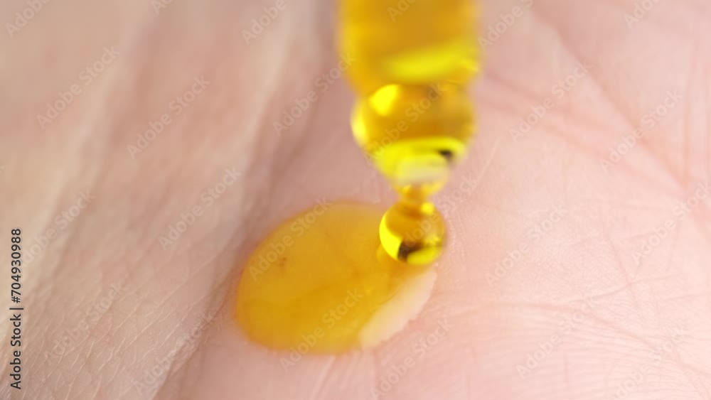 Closeup of yellow serum gel or oil falling on the skin. Macro shot of transparent orange serum gel in pipette falling on the palm