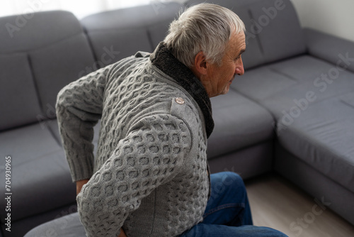 Elderly man near sofa with cactus at home. Hemorrhoids concept photo