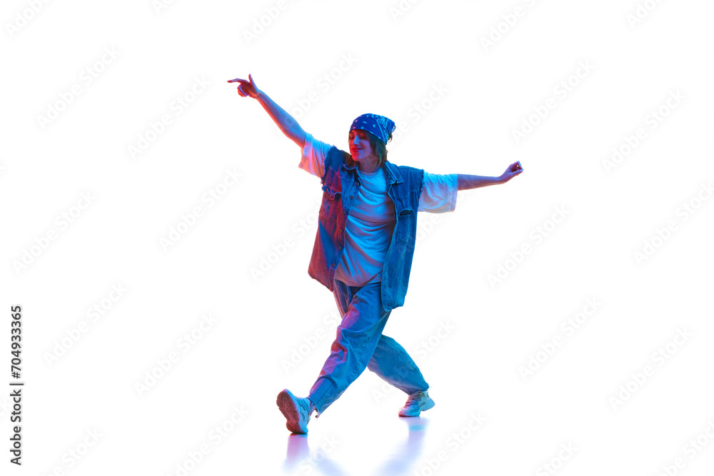 Sportive young woman in casual jeans sportive clothe dancing modern dance isolated over white background in neon light. Concept of contemporary dance, street style, youth, hobby, action, lifestyle