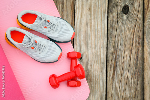 Karemat, sneakers and dumbbells on wooden background, space for text
