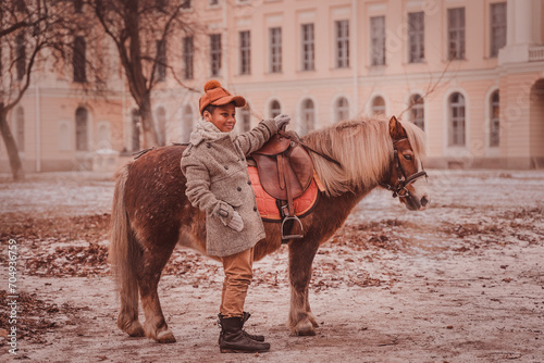 smiling boy stands next to a pony holding the pommel of the saddle