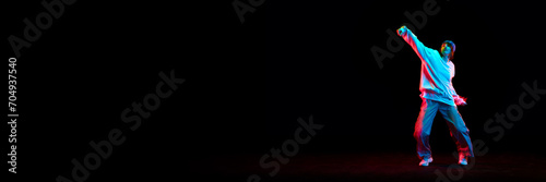 Young girl, hip hop dancer in motion, dancing isolated over black background in neon light. Concept of contemporary dance, street style, youth, hobby, lifestyle. Banner. Empty space to insert text