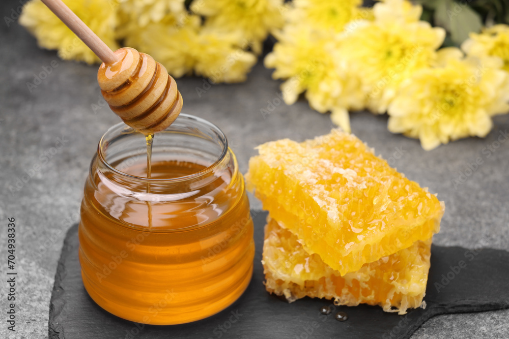Pouring sweet golden honey from dipper into jar and pieces of honeycomb on grey table Pouring sweet golden honey from dipper into jar and pieces of honeycomb on grey table