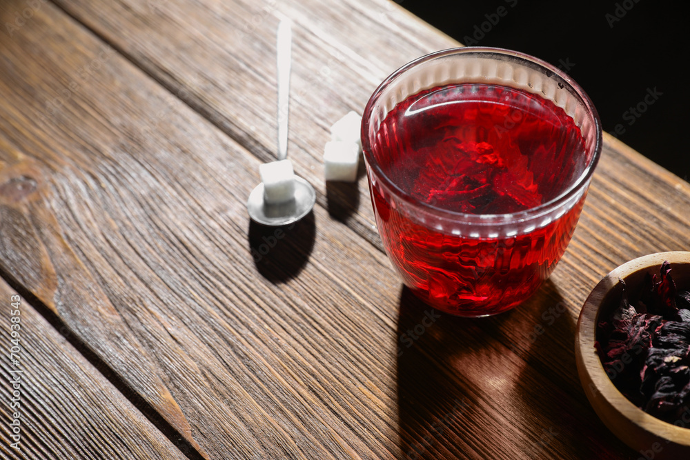 Delicious hibiscus tea in glass, sugar cubes and dry roselle petals on wooden table, above view. Space for text Delicious hibiscus tea in glass, sugar cubes and dry roselle petals on wooden table, above view. Space for text