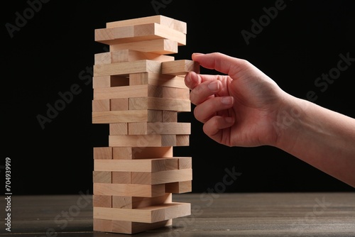 Woman playing Jenga at table against black background, closeup