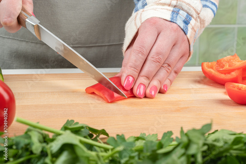 Female hands with manicure cut a piece of sweet pepper on a wooden cutting board.
