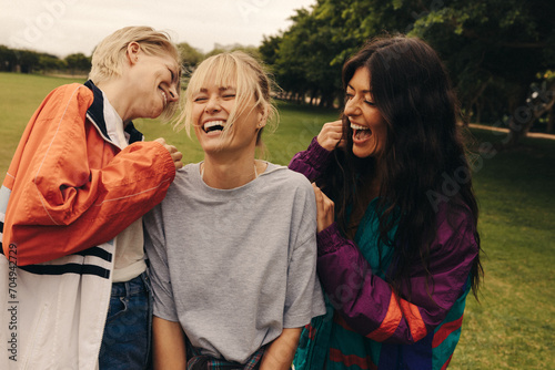 Three female friends laughing and bonding outdoors in a casual park hangout photo