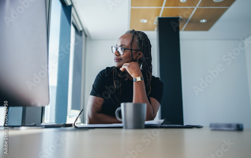 Black business woman looking away and thinking while sitting in her office photo