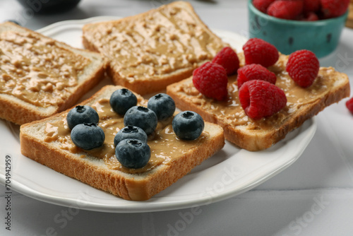 Delicious toasts with peanut butter, raspberries and blueberries on white table, closeup