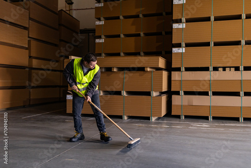 Portrait of young man with Down syndrome sweeping the floor, working in factory, warehouse. Concept of workers with disabilities, support in workplace. photo
