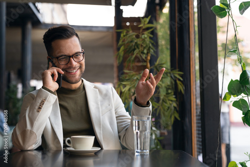 Happy wealthy successful young business man talking on the phone in Cafe. Smiling professional businessman executive entrepreneur wearing suit making corporate call on cellphone. photo