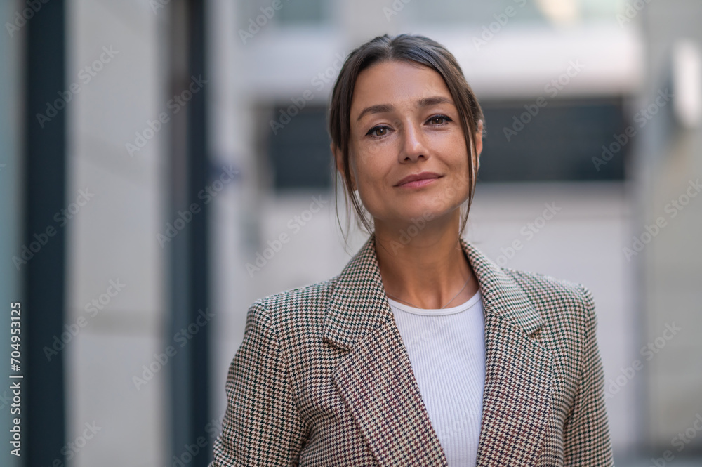 Woman wearing beige suit posing near urban building.
