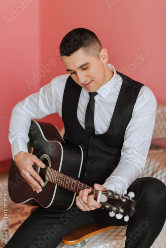 The groom sings songs to the guitar in the morning in his room. Groom in a black suit. Happy man. Preparation for the wedding.
