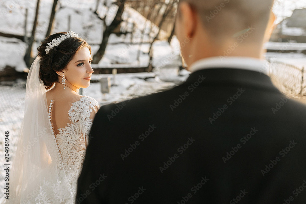 Naklejka premium Winter wedding. A happy couple in wedding clothes are hugging and smiling in a winter park covered with snow on their wedding day. Winter love story of a beautiful couple in snowy winter weather