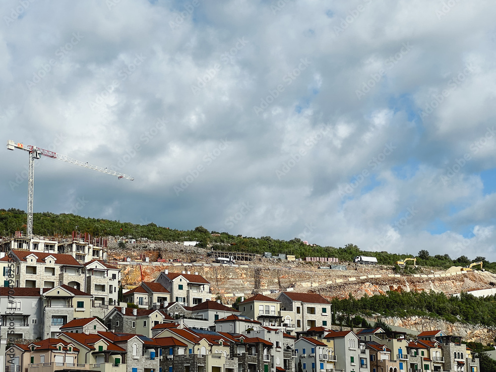 Construction crane over colorful buildings with red roofs on a mountain slope