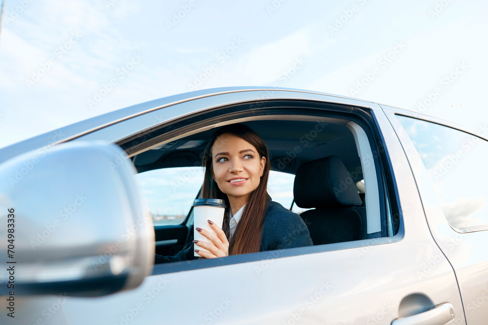 Beautiful woman holding steering wheel and coffee cup while driving a car. Happy young woman with coffee to go driving her car.