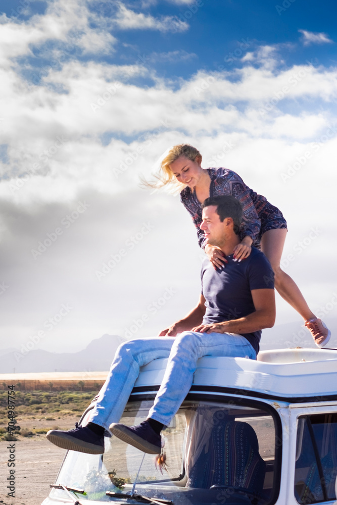 Happy couple enjoy the roof van together having fun in travel holiday alternative vacation - people together in road trip with transport vehicle and love life concept with sky  in background freedom