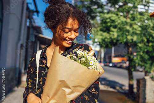 Young smiling afro american woman walks along the street with a bouquet of daisies.