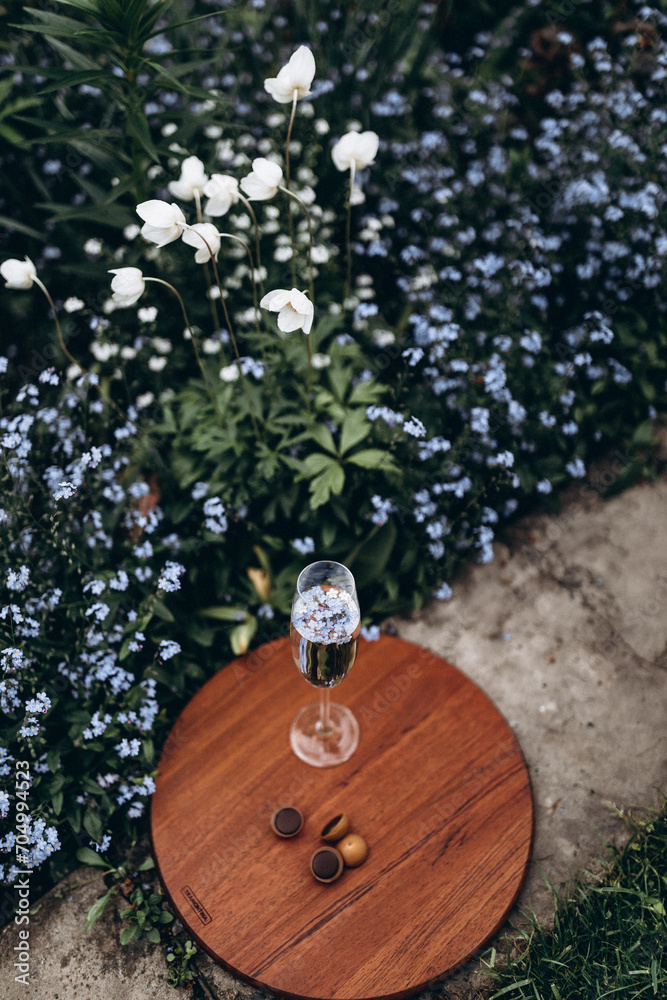 A glass stands on a wooden stand in the midst of a garden lawn and flowerbeds