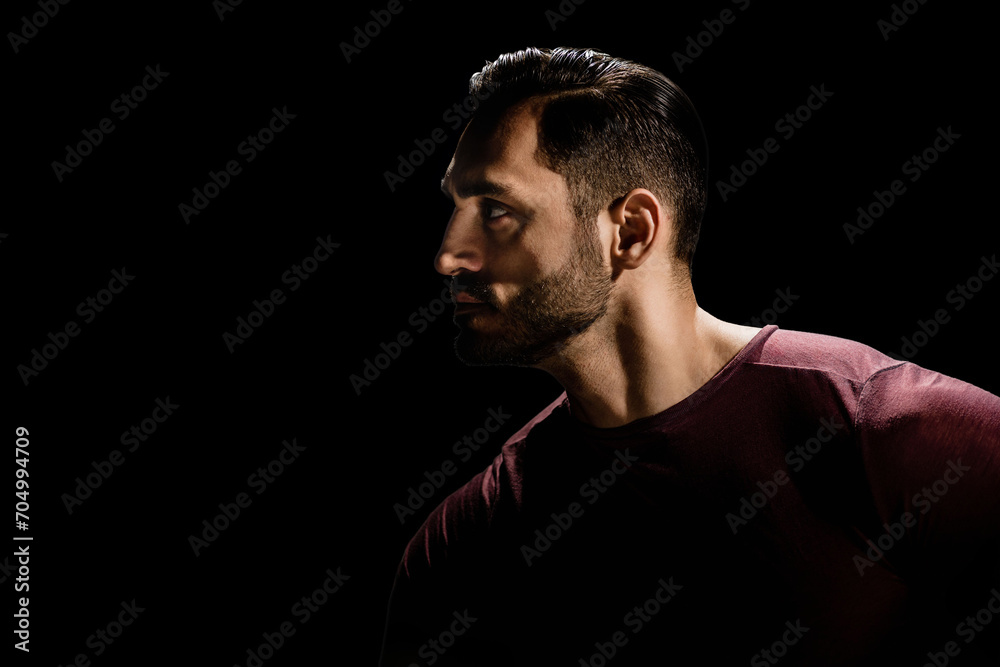 Low key portrait of young man with beard on dark background, Dramatic ambiance: Young man's portrait exudes intensity in low-key darkness