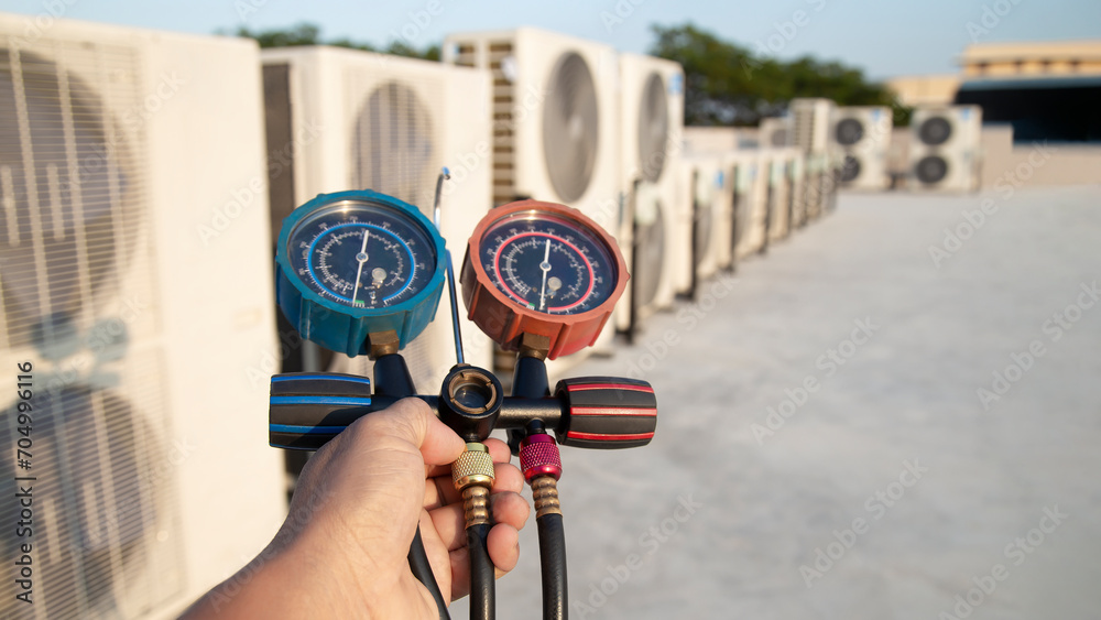 Air conditioning, HVAC service technician using gauges to check refrigerant and add refrigerant.	