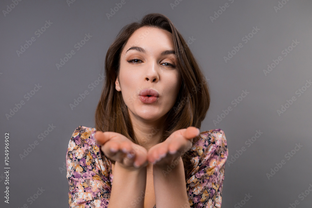A young woman blows a kiss to the camera. Studio photo shoot on a gray background