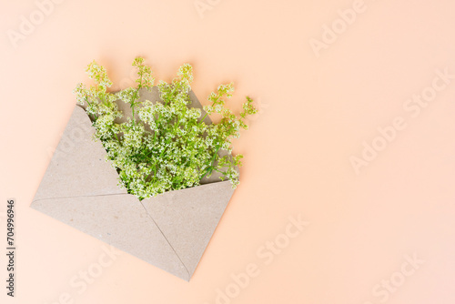 Natural background on beige color with opened paper envelope and bouquet of white littlr spring wild flowers insid of it.Concept of spring coming, holidays, good news and love emotion.Copy space
