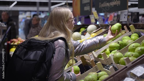 Young schoolgirl picks the pear in the grocery store. Teen girl with backpack. Healthy eating habits.