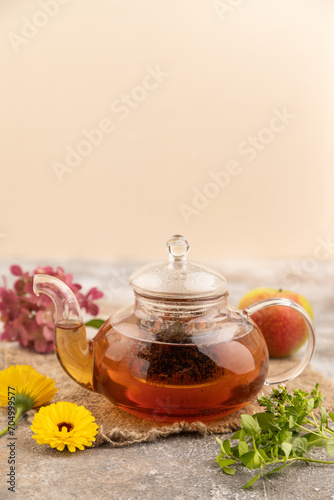 Red tea with herbs in glass teapot on brown concrete. Side view, selective focus.