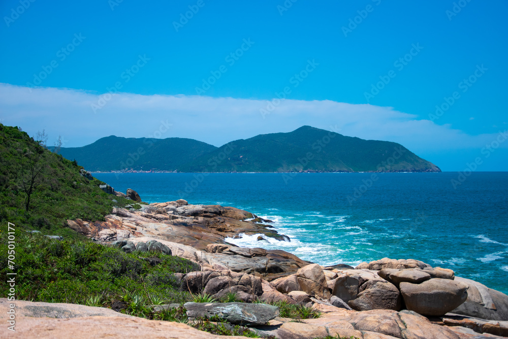 The picture shows a rocky coastline with turquoise-green water, green slopes and an absolutely blue sky without clouds.
