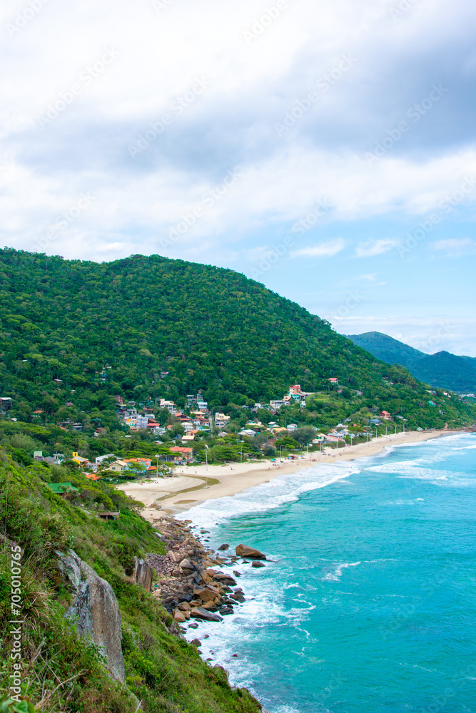 The view extends to a long sandy beach surrounded by green, densely vegetated mountains and turquoise sea. Solidão Beach, Florianópolis, Brazil