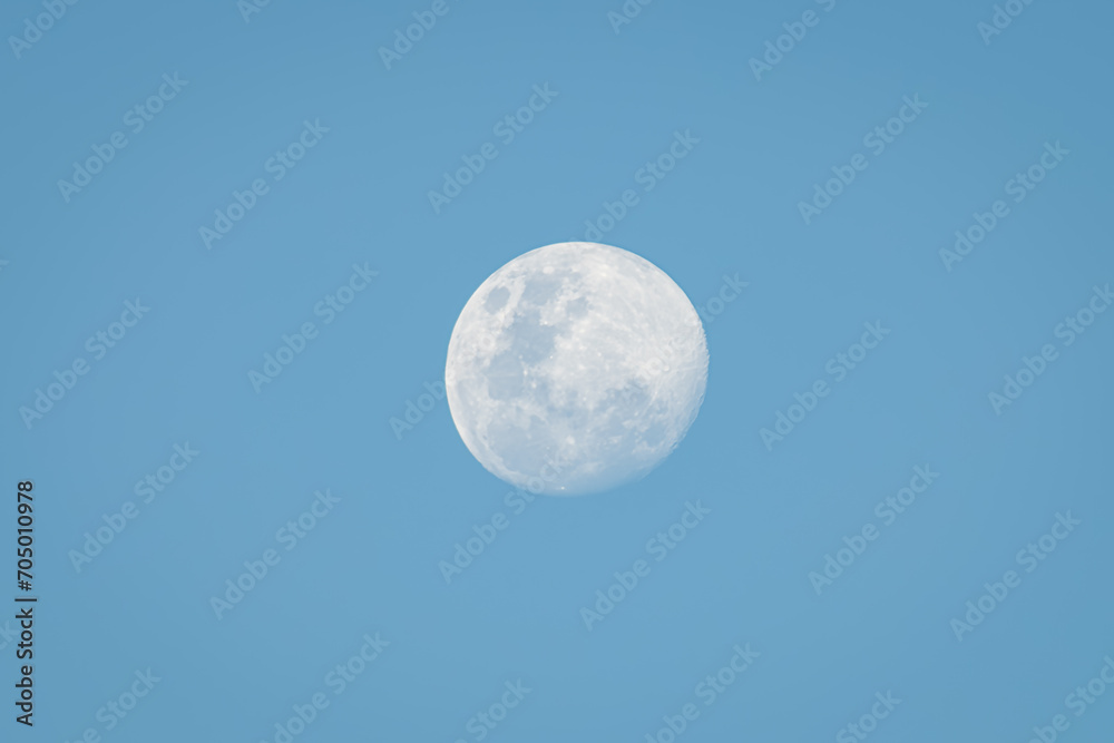 White full moon against blue sky, with clear sky and moon details.