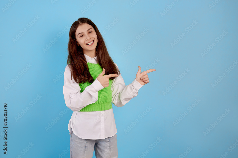 Young brunette teenage girl showing aside by hands on blue background. Copyspace on the right Young brunette teenage girl showing aside by hands on blue background. Copyspace on the right