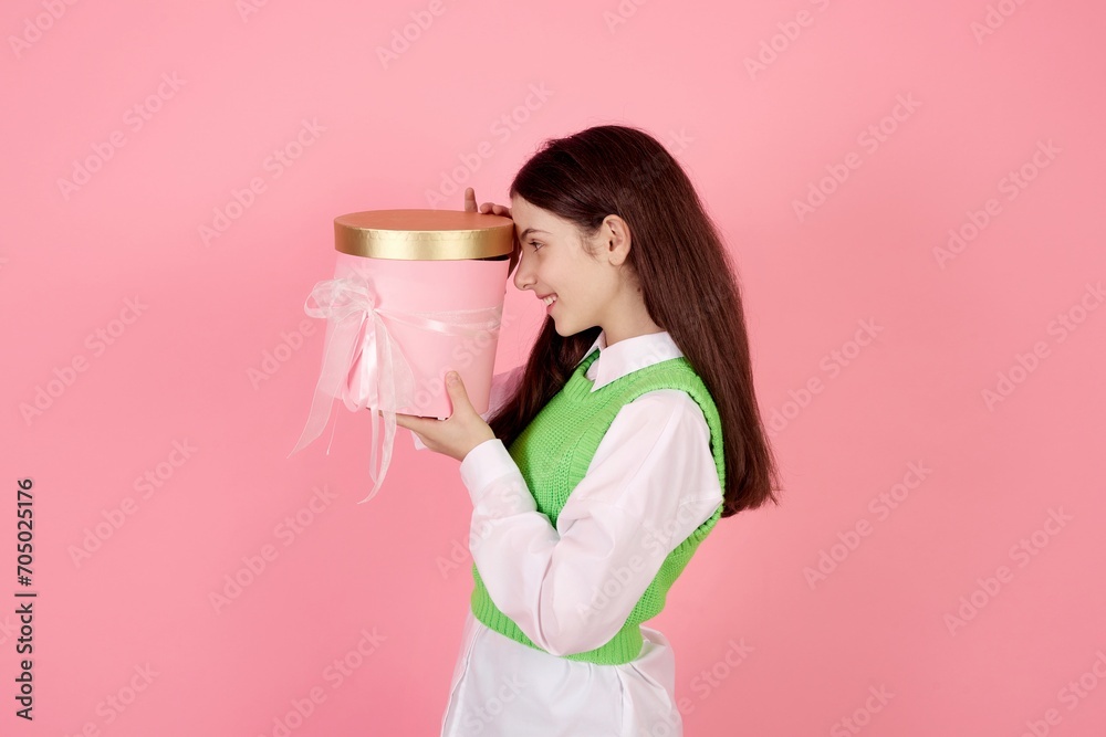 Smiling teenage girl holding present box and looking inside on pink background in studio. Smiling teenage girl holding present box and looking inside on pink background in studio.