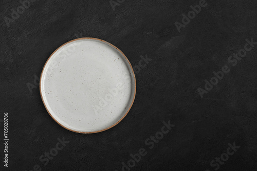 Handmade empty ceramic plate top view with copy space on dark concrete table. Minimalism. Eco friendly ceramics handcraft tableware.