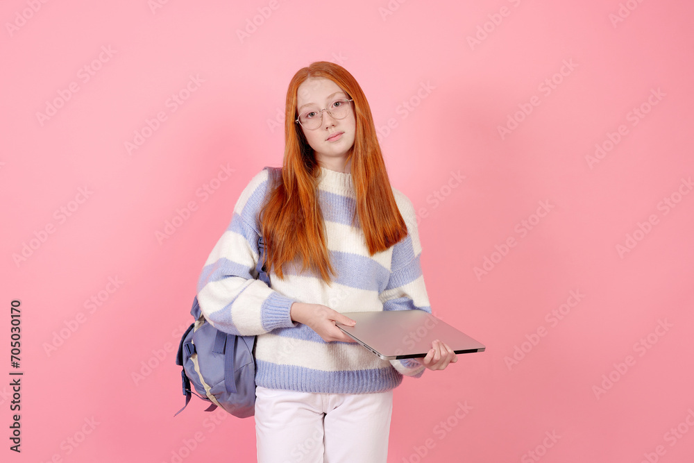 Confident redhead teenage girl with bag and laptop wearing glasses on pink background in studio. Confident redhead teenage girl with bag and laptop wearing glasses on pink background in studio.
