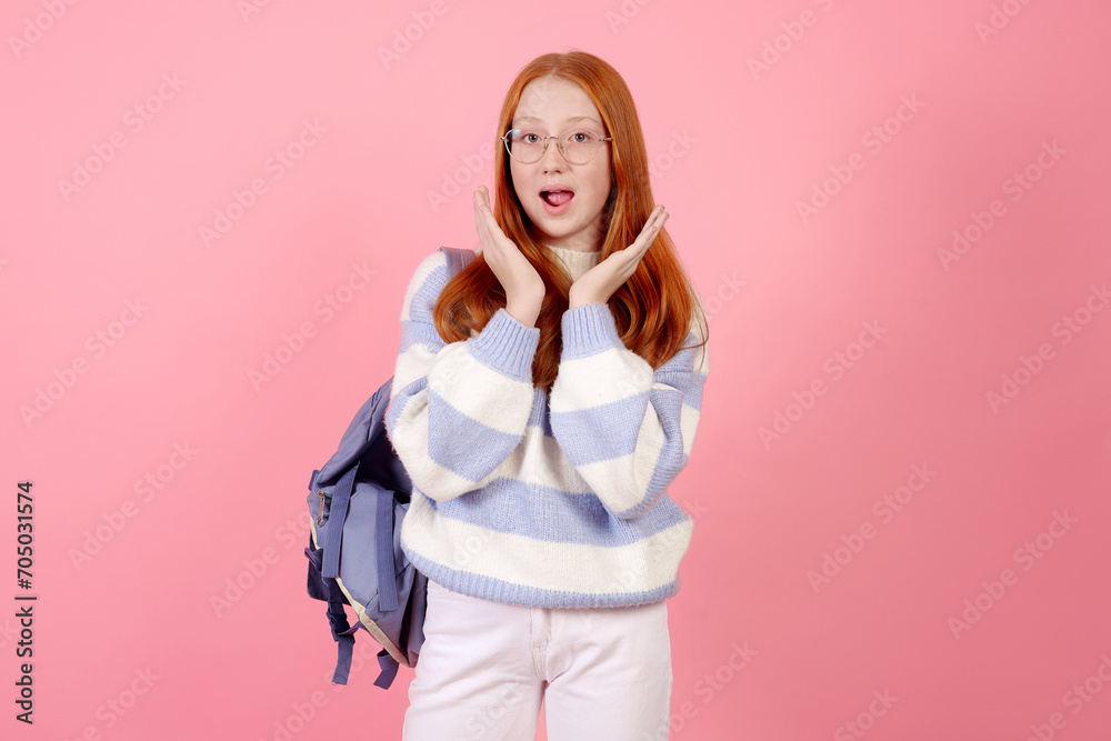 Surprised redhead teenage girl with bag wearing glasses on pink background in studio. Surprised redhead teenage girl with bag wearing glasses on pink background in studio.