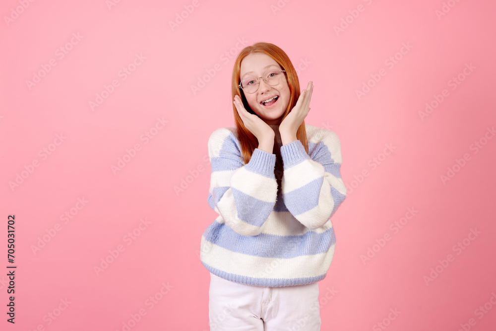 Surprised redhead teenage girl wwearing glasses and point by finger on copy space on pink background in studio. Surprised redhead teenage girl wwearing glasses and point by finger on copy space on pink background in studio.