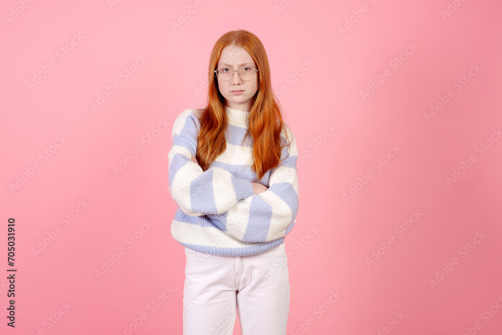 Confident redhead teenage girl wearing glasses and sweater on pink background in studio. Confident redhead teenage girl wearing glasses and sweater on pink background in studio.