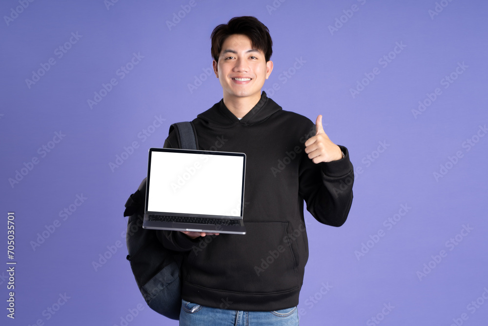 Asian male student using laptop on purple background
