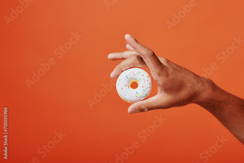 Fototapeta Naklejka Na Ścianę i Meble -  cropped shot of person holding glazed vanilla donut with sprinkles on orange background, white icing