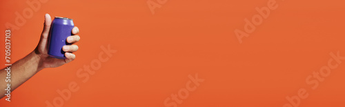 cropped banner of person holding purple soda can in hand on orange background, carbonated drink