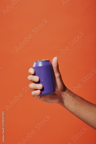 cropped photo of person holding purple soda can in hand on orange background, carbonated drink